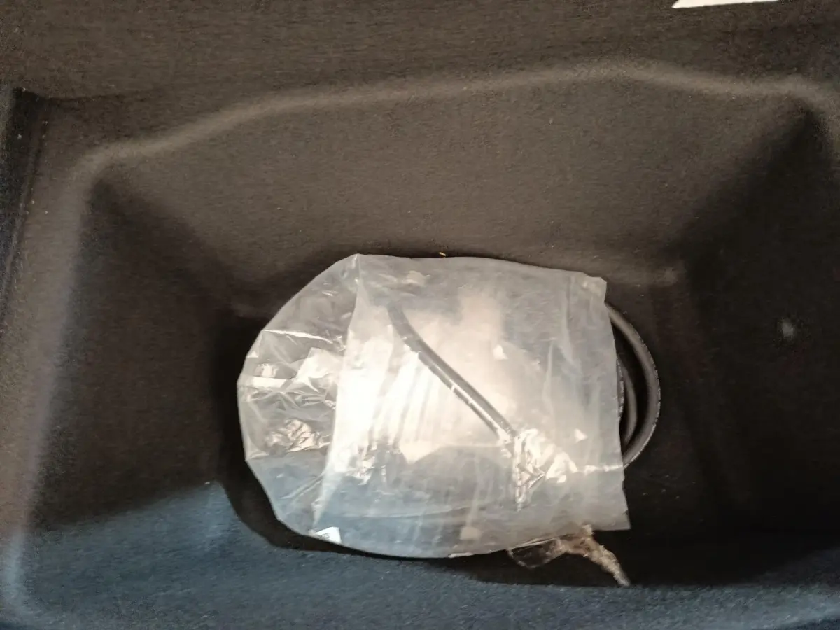 Gros plan sur le coffre avant noir d'une Tesla Model 3 blanche, montrant un câble de recharge emballé.