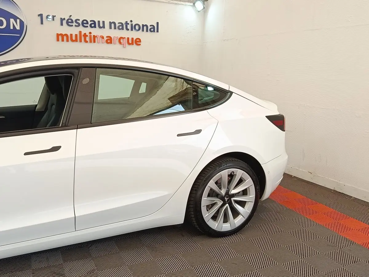 Profil arrière droit d'une Tesla Model 3 blanche 2022, avec jantes distinctives et vitres teintées.