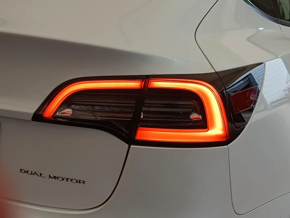 Gros plan sur le feu arrière droit allumé d'une Tesla Model 3 blanche avec logo Dual Motor visible.