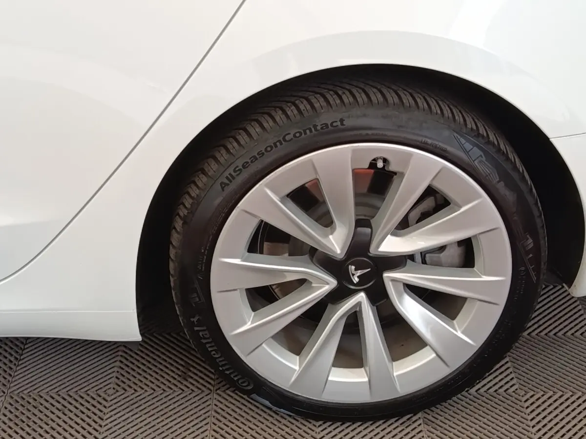 Gros plan sur la roue arrière droite blanche d'une Tesla Model 3 Grande Autonomie avec jante argentée distinctive.