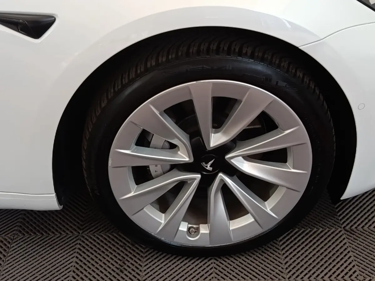 Gros plan sur la roue avant gauche argentée d'une Tesla Model 3 blanche, mettant en valeur la jante au design aérodynamique.