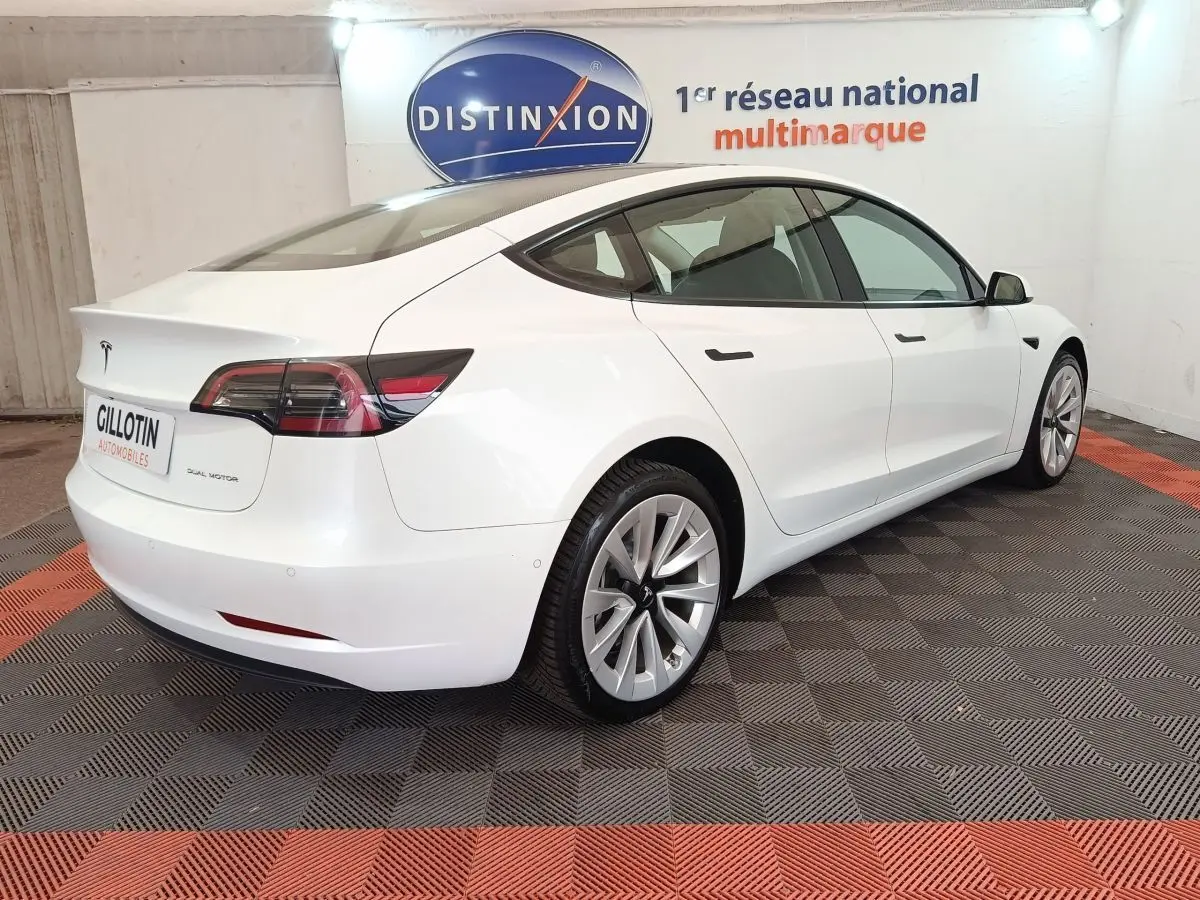 Tesla Model 3 Grande Autonomie blanc vue 3/4 arrière droit dans un showroom avec logo Distinxion en arrière-plan.