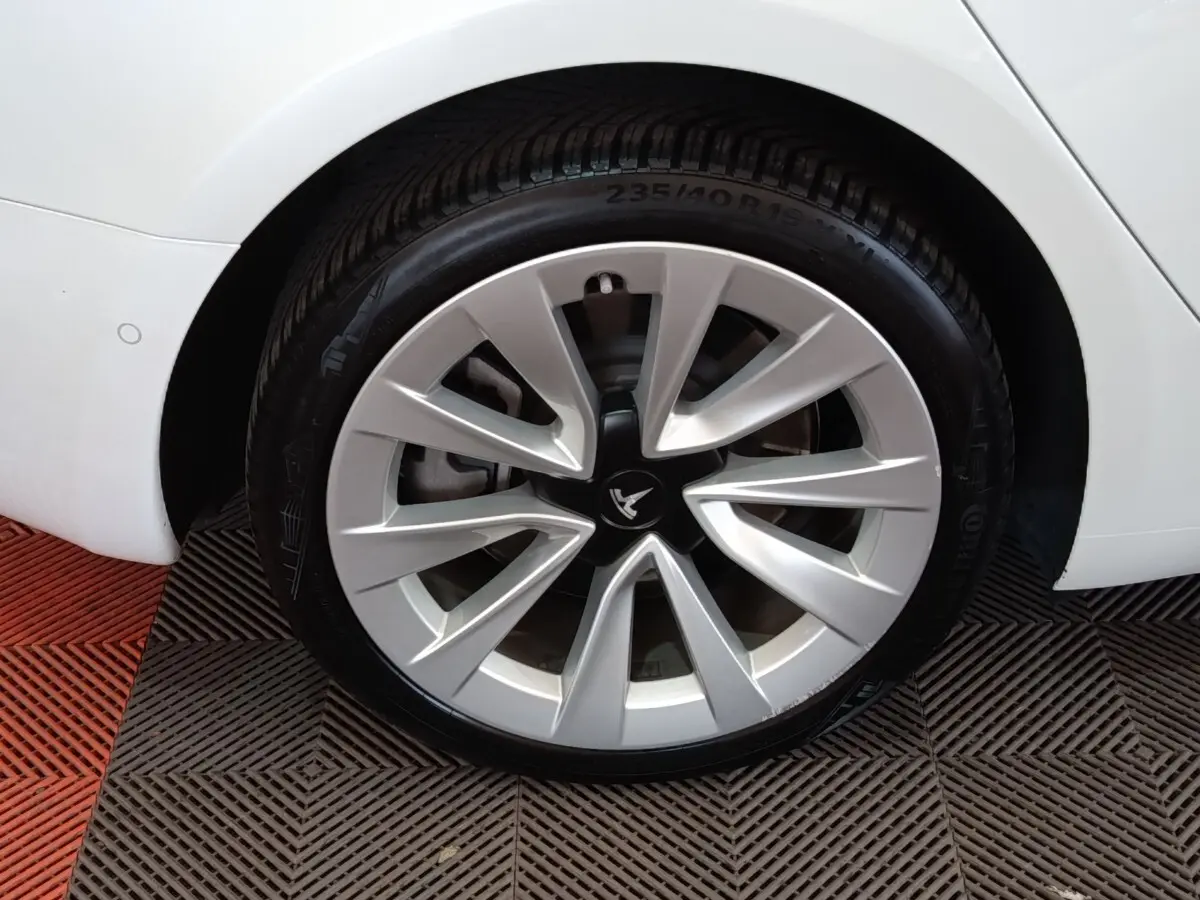 Gros plan sur la roue arrière droite d'une Tesla Model 3 blanche, mettant en valeur la jante aérodynamique distinctive.
