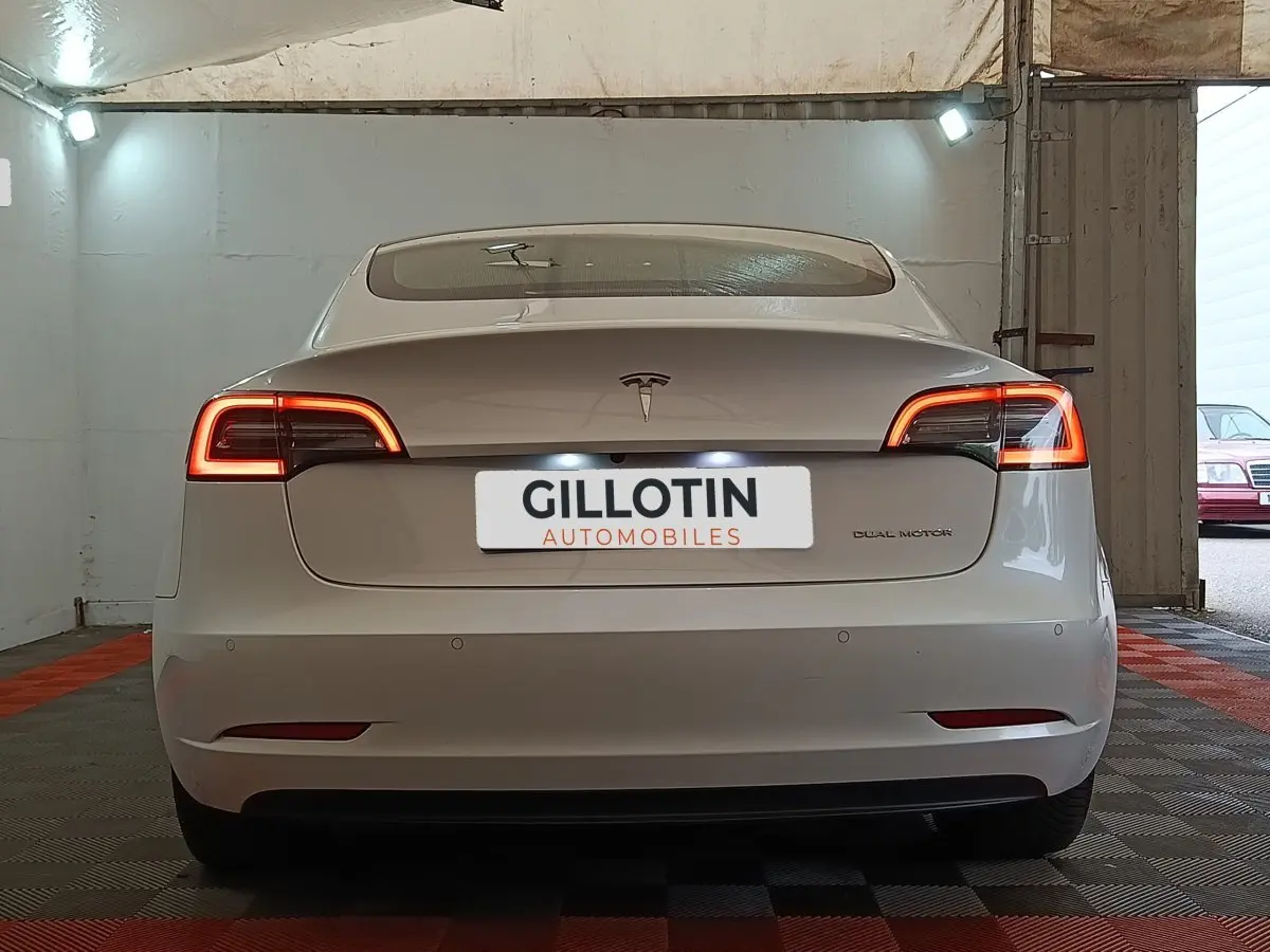 Vue arrière d'une Tesla Model 3 Grande Autonomie blanche avec feux LED allumés dans un garage.