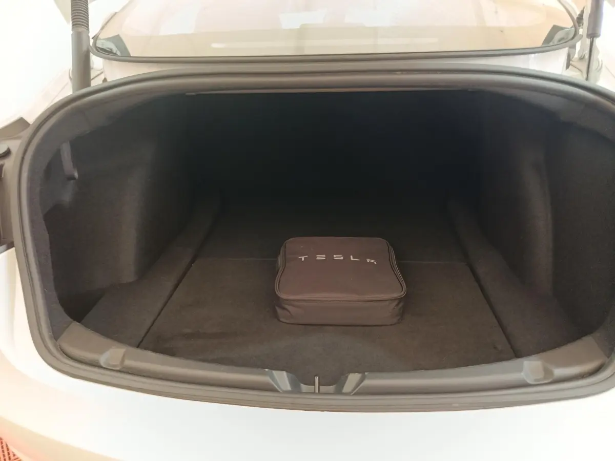 Coffre ouvert d'une Tesla Model 3 blanche 2022, vue de face, avec sac de rangement Tesla noir à l'intérieur.