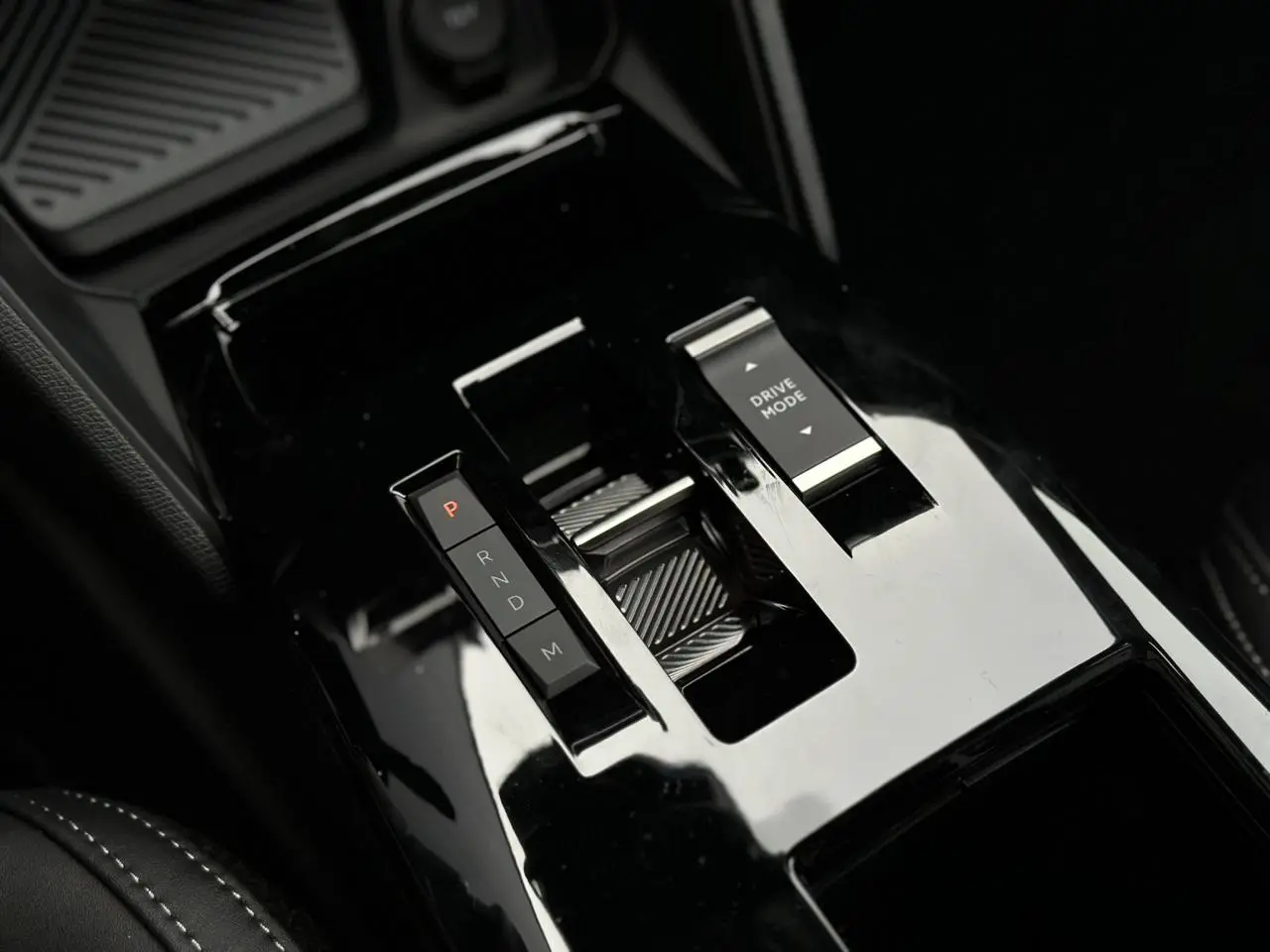 Gros plan sur la console centrale noire brillante du Citroën C4 NV Hybrid 145 e-DSC6 Max avec commandes de boîte auto et mode de conduite.