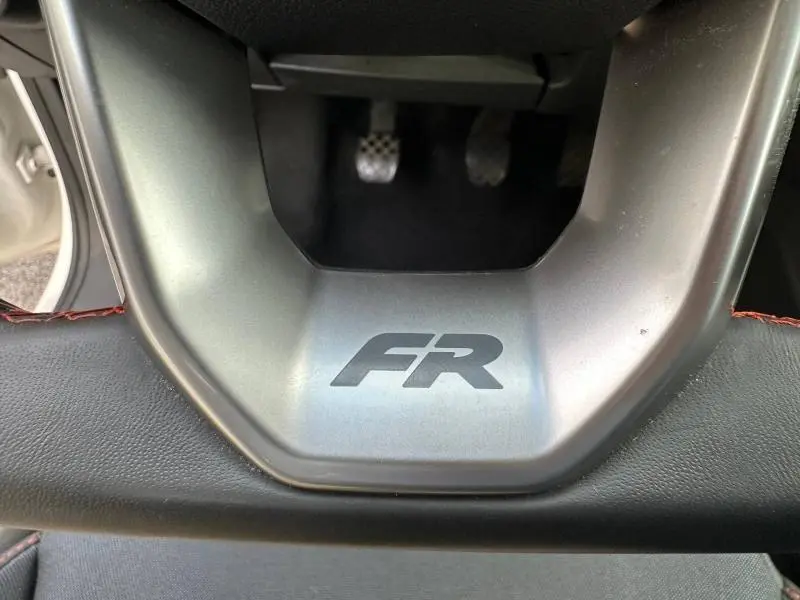 Détail du volant avec logo FR en gris sur fond métal, pédales sport en arrière-plan dans une SEAT Ibiza 2025 blanc Nevada.