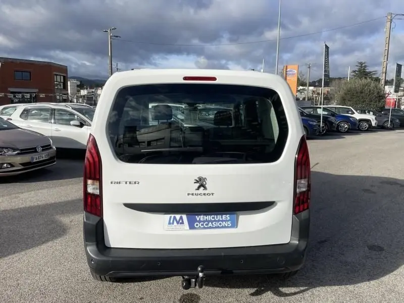 Vue arrière d'un Peugeot Rifter blanc 2020 avec hayon fermé et attelage visible sur un parking extérieur.