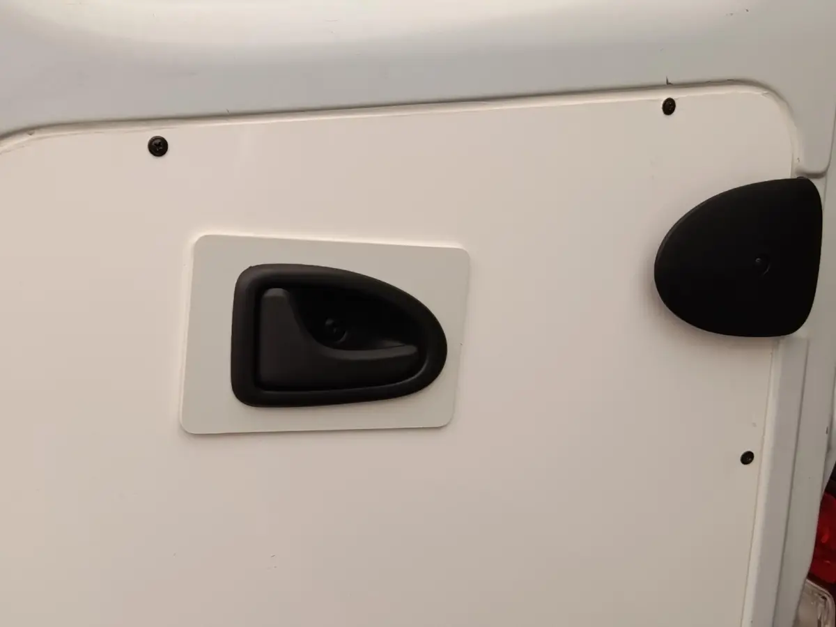Gros plan sur la poignée de porte arrière noire d’un Renault Trafic Fourgon blanc, vue latérale droite.
