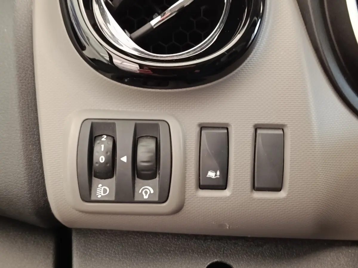 Gros plan sur les commandes de réglage des phares et de l'ESP sur le tableau de bord gris clair du Renault Trafic Fourgon blanc.