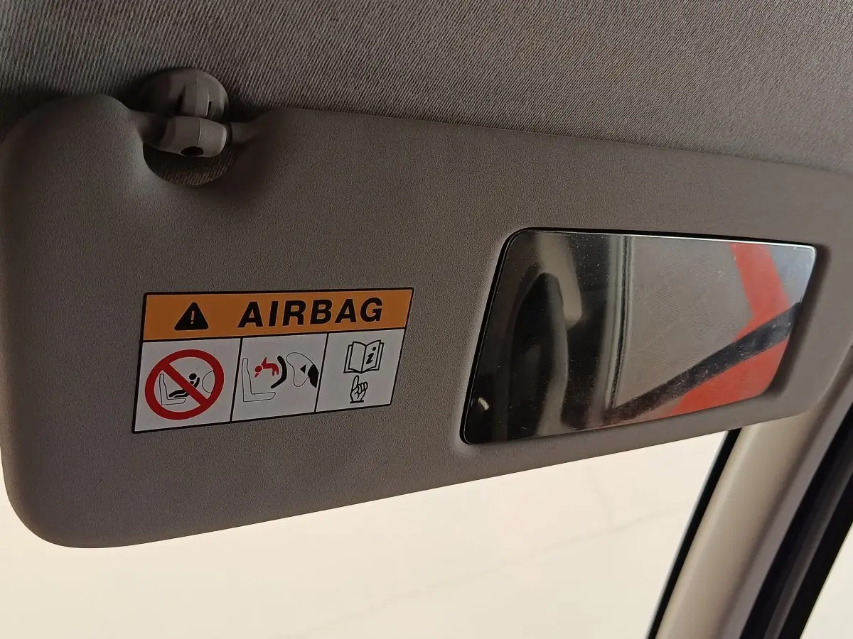 Détail du pare-soleil côté conducteur beige avec miroir et étiquette d'avertissement airbag dans un Renault Trafic blanc.