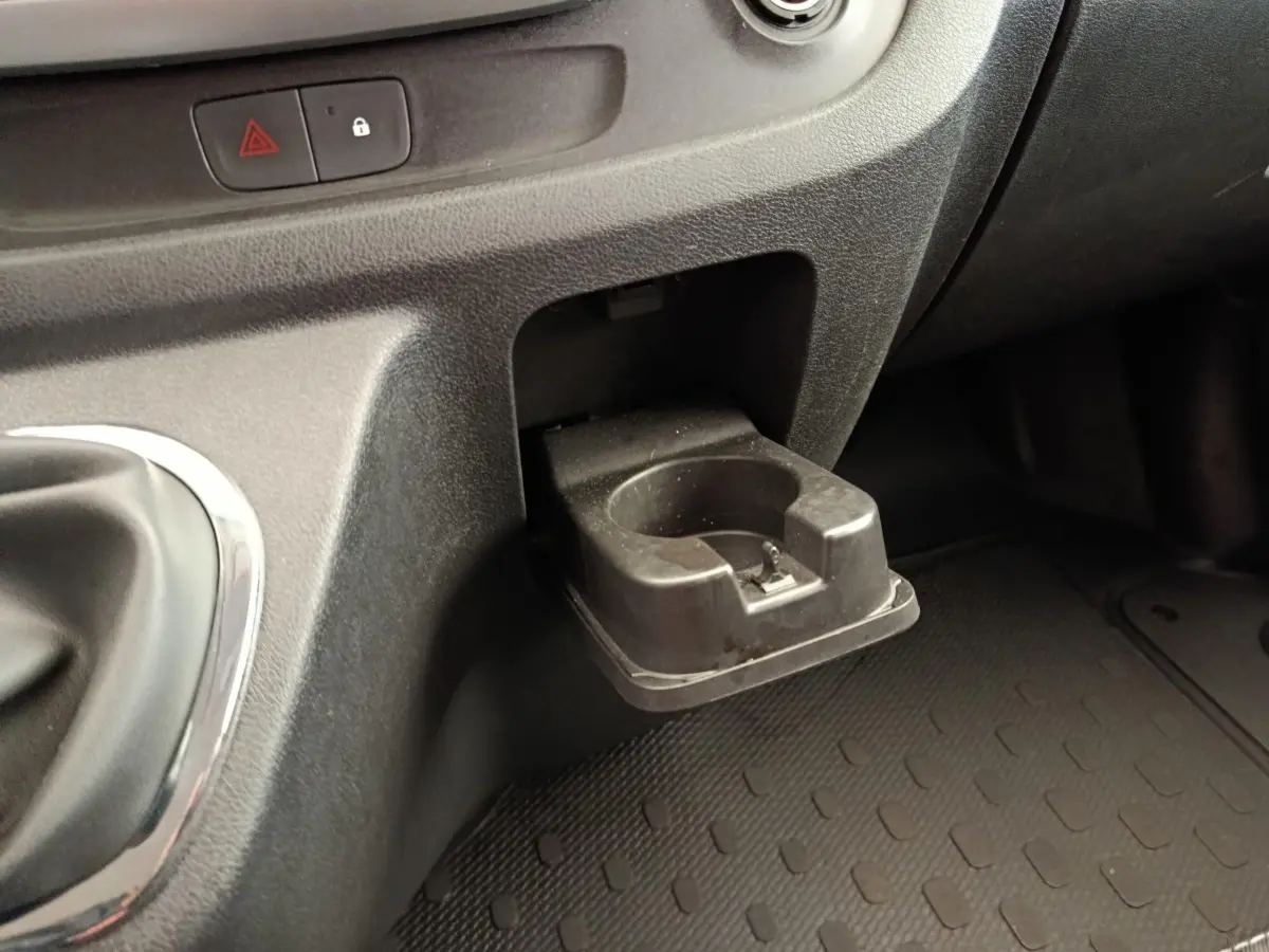 Gros plan sur le porte-gobelet noir escamotable côté passager du tableau de bord du Renault Trafic blanc.