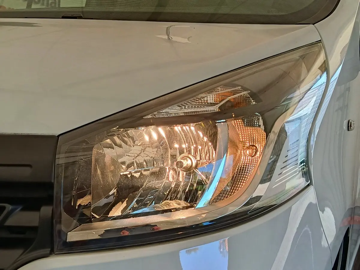 Gros plan sur le phare avant droit du Renault Trafic blanc, mettant en valeur le design halogène et la carrosserie brillante.