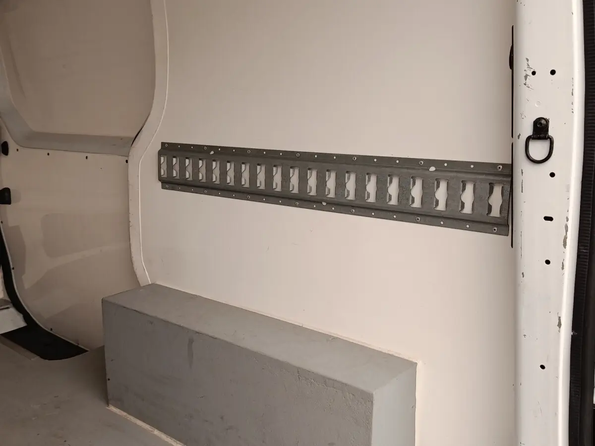 Vue intérieure côté droit du fourgon blanc Renault Trafic, montrant la cloison pleine et un rail métallique mural.