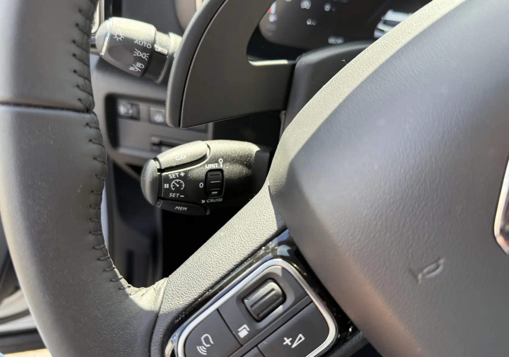 Gros plan sur la commande de régulateur de vitesse à gauche du volant gris du Citroën C5 Aircross Hybrid 2025.