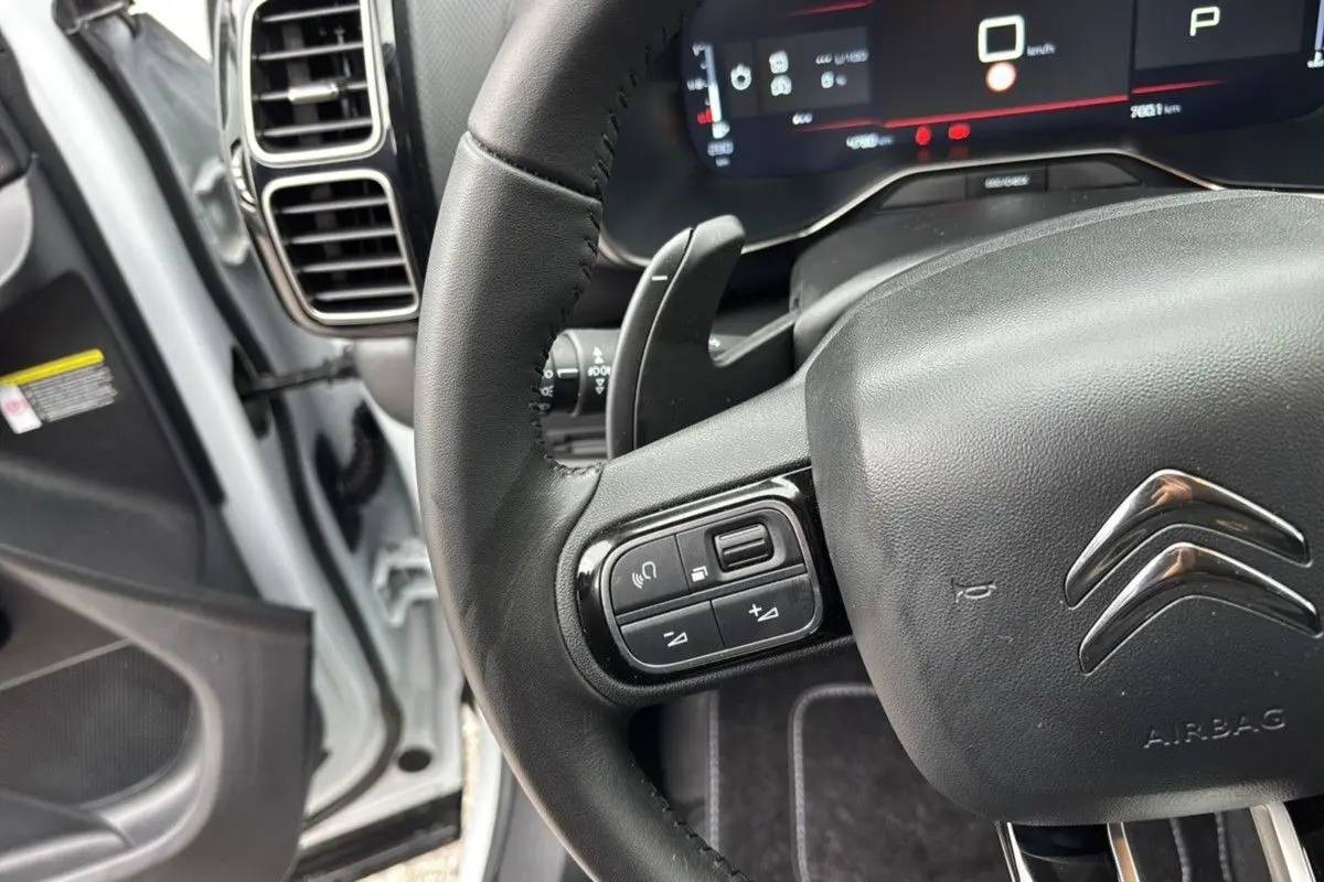 Vue rapprochée du volant noir du Citroën C5 Aircross Hybrid 2025, avec commandes intégrées et tableau de bord numérique visible.