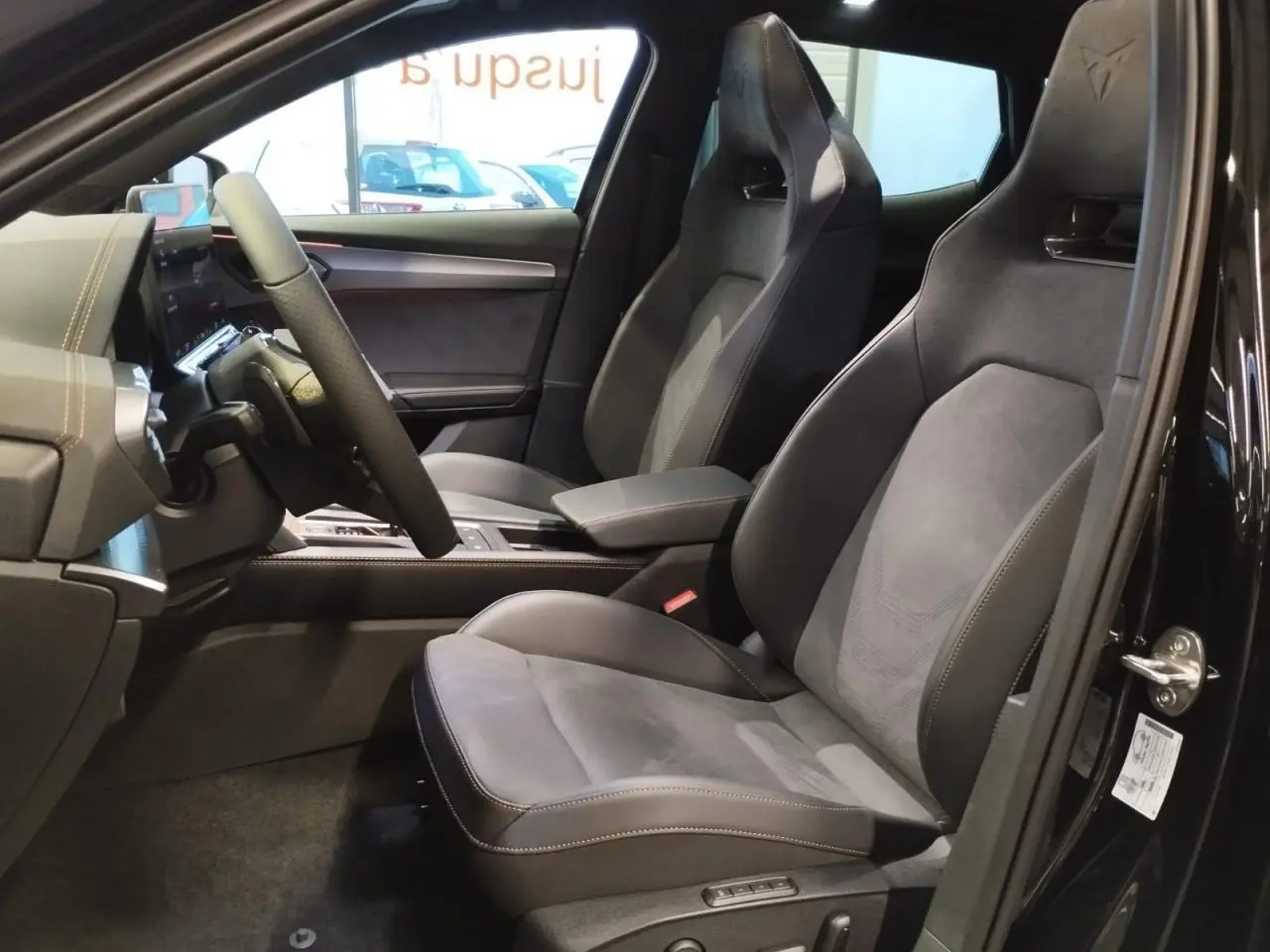 Vue intérieure côté conducteur du CUPRA Formentor noir métal 2026, sièges baquets suédine avec surpiqûres cuivrées et logo Cupra sur appuie-tête.