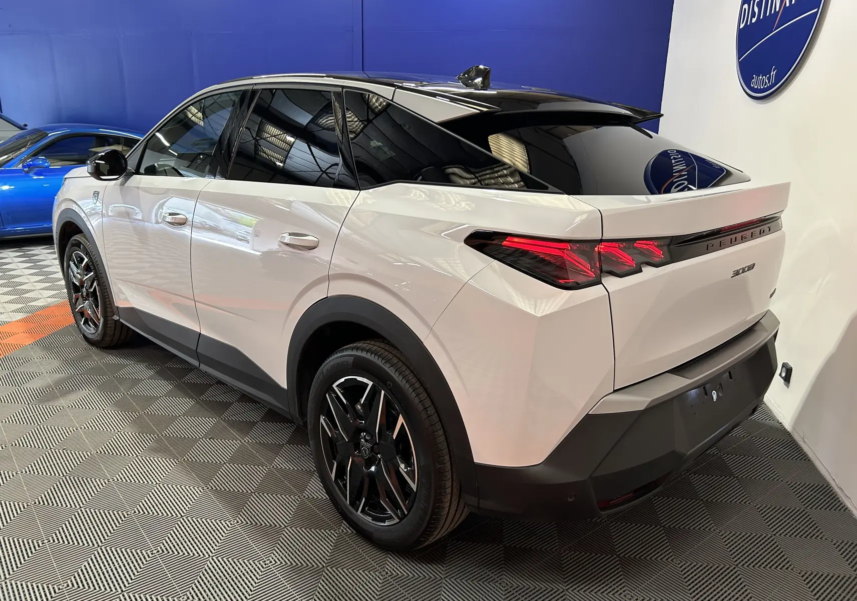Vue 3/4 arrière droite du Peugeot 3008 Hybrid blanc Okenite avec toit noir et jantes noires en intérieur showroom.