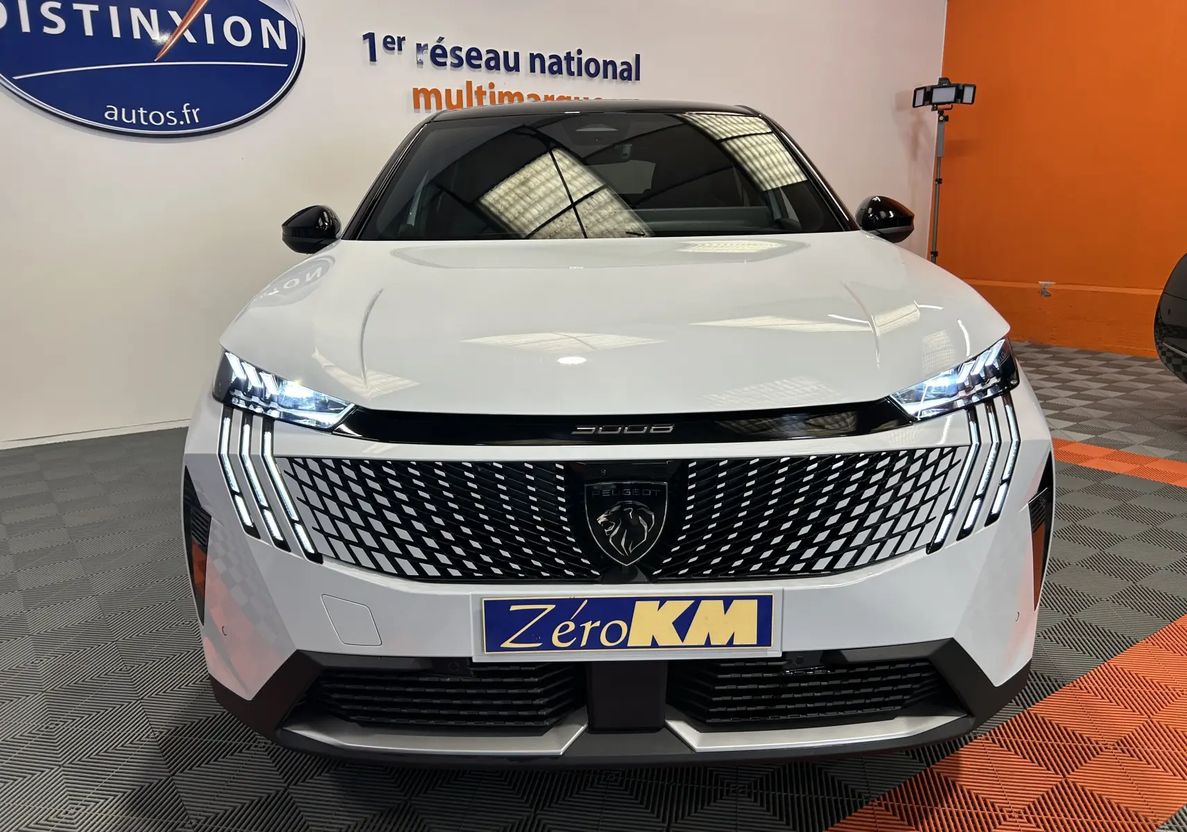 Vue frontale du Peugeot 3008 III Hybrid blanc Okenite avec calandre distinctive et feux LED allumés en showroom.