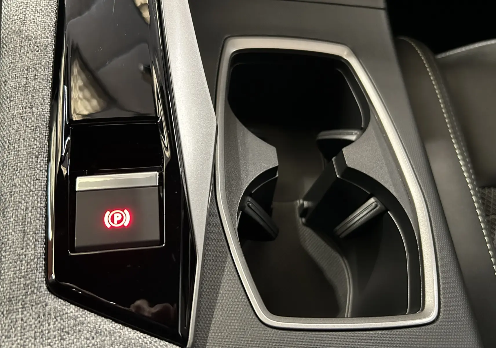 Gros plan intérieur sur la console centrale noire et grise du Peugeot 3008 Hybrid avec bouton de frein à main électronique allumé.