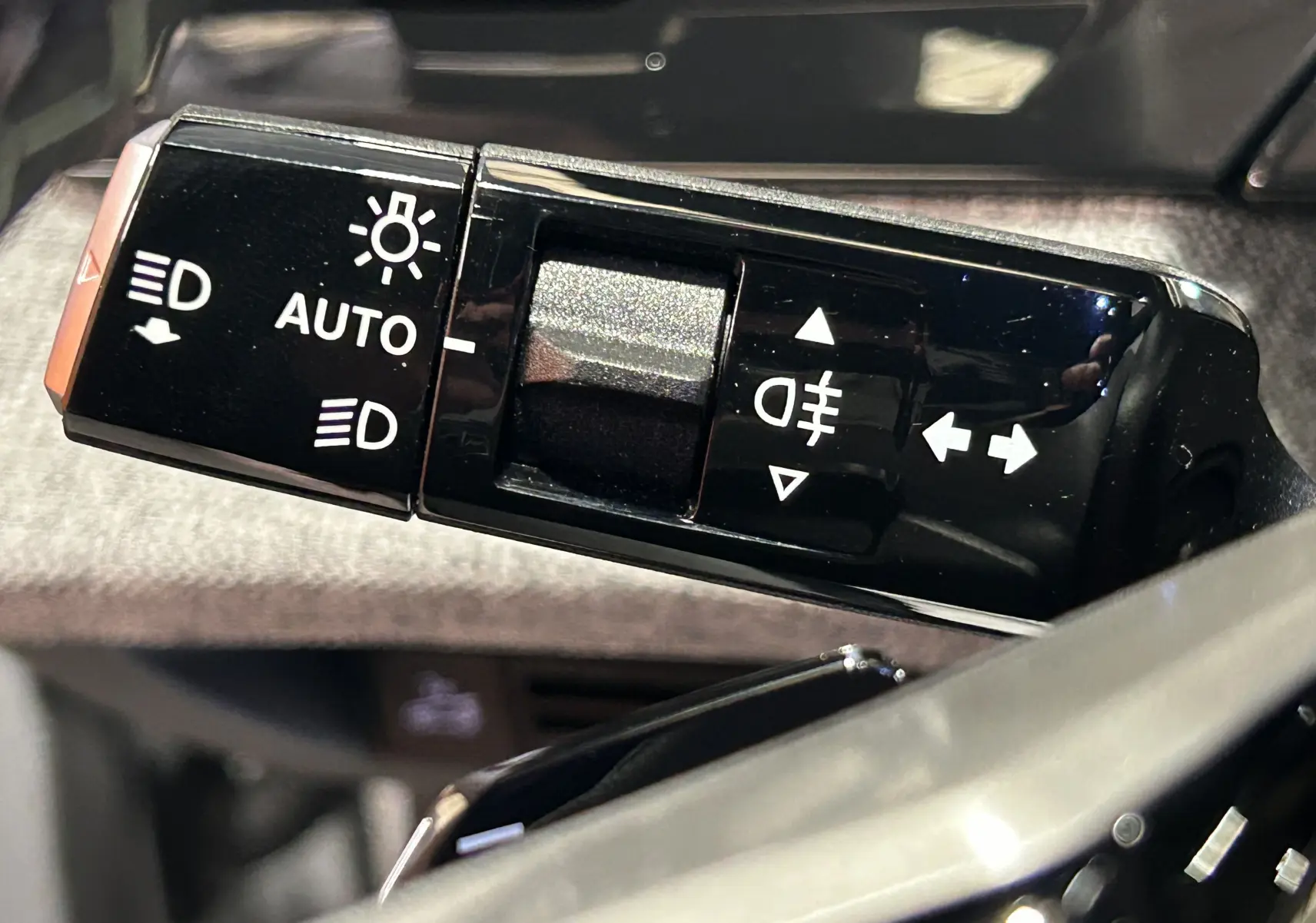 Gros plan sur la commande de phares et clignotants noire dans l’habitacle du Peugeot 3008 Hybrid blanc Okenite.
