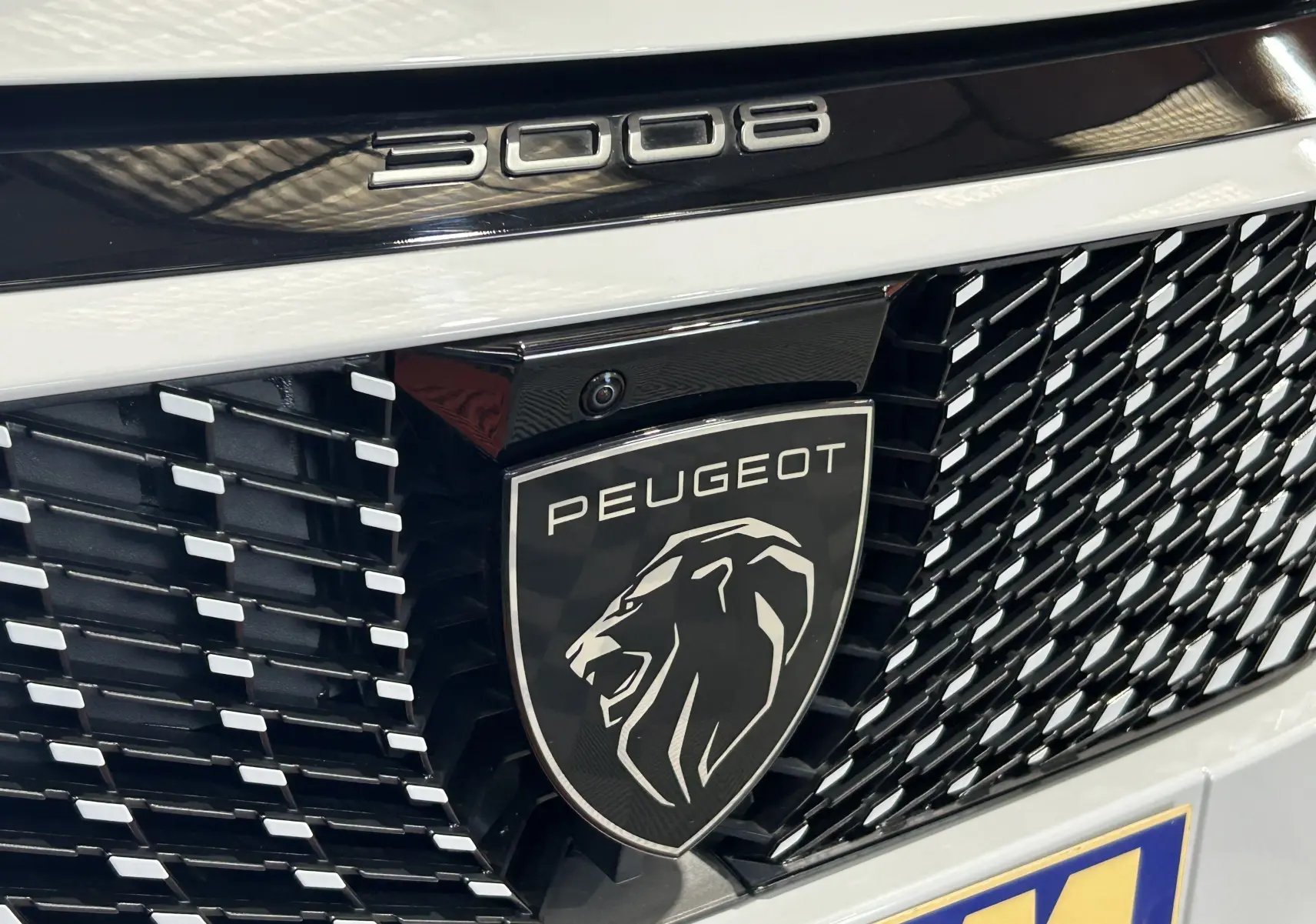 Gros plan sur la calandre noire et blanche du Peugeot 3008 Hybrid 145 GT avec logo lion et inscription 3008.