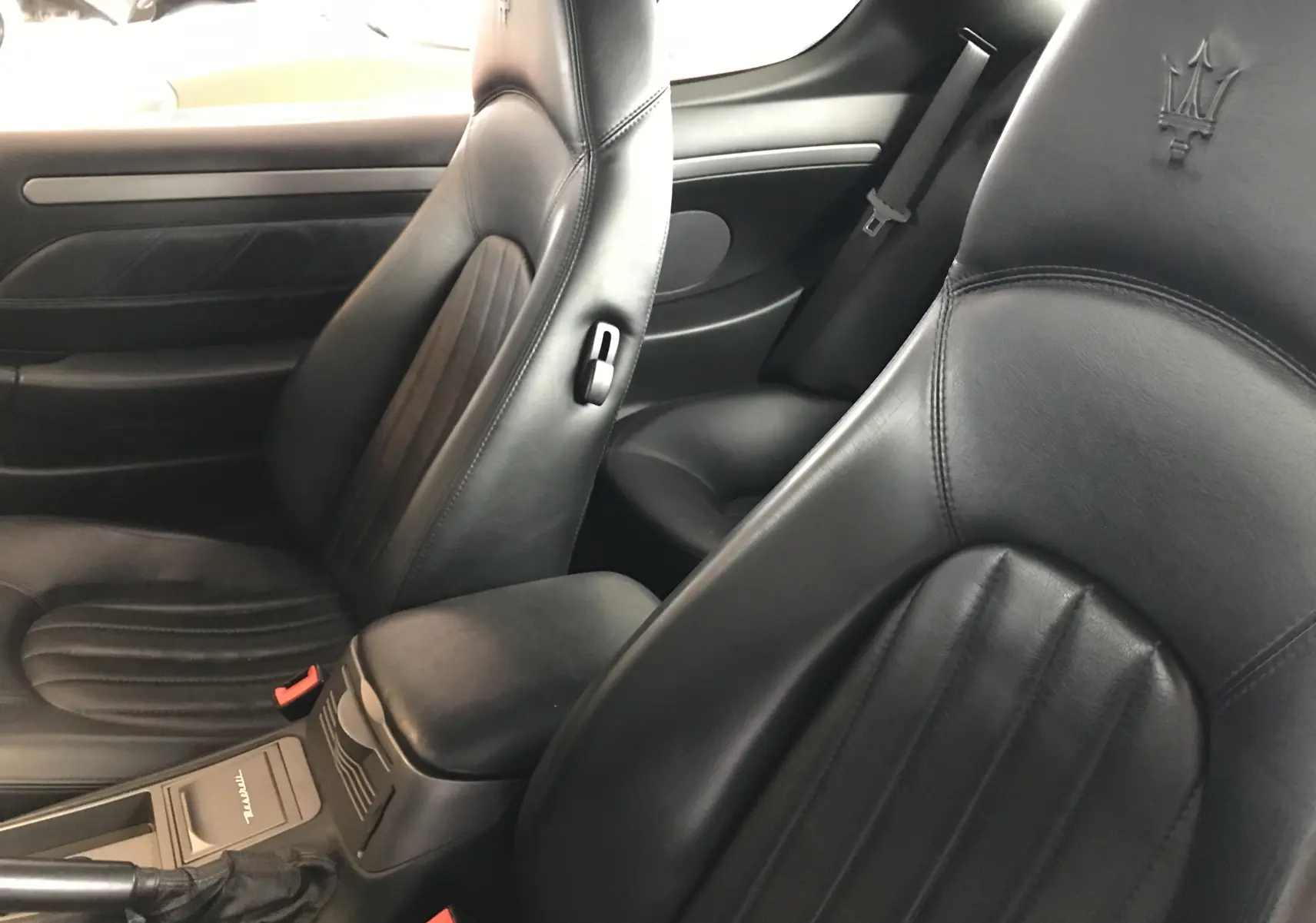 Gros plan sur les sièges avant en cuir noir de la Maserati Coupé 4.2l V8, mettant en valeur le logo trident brodé.