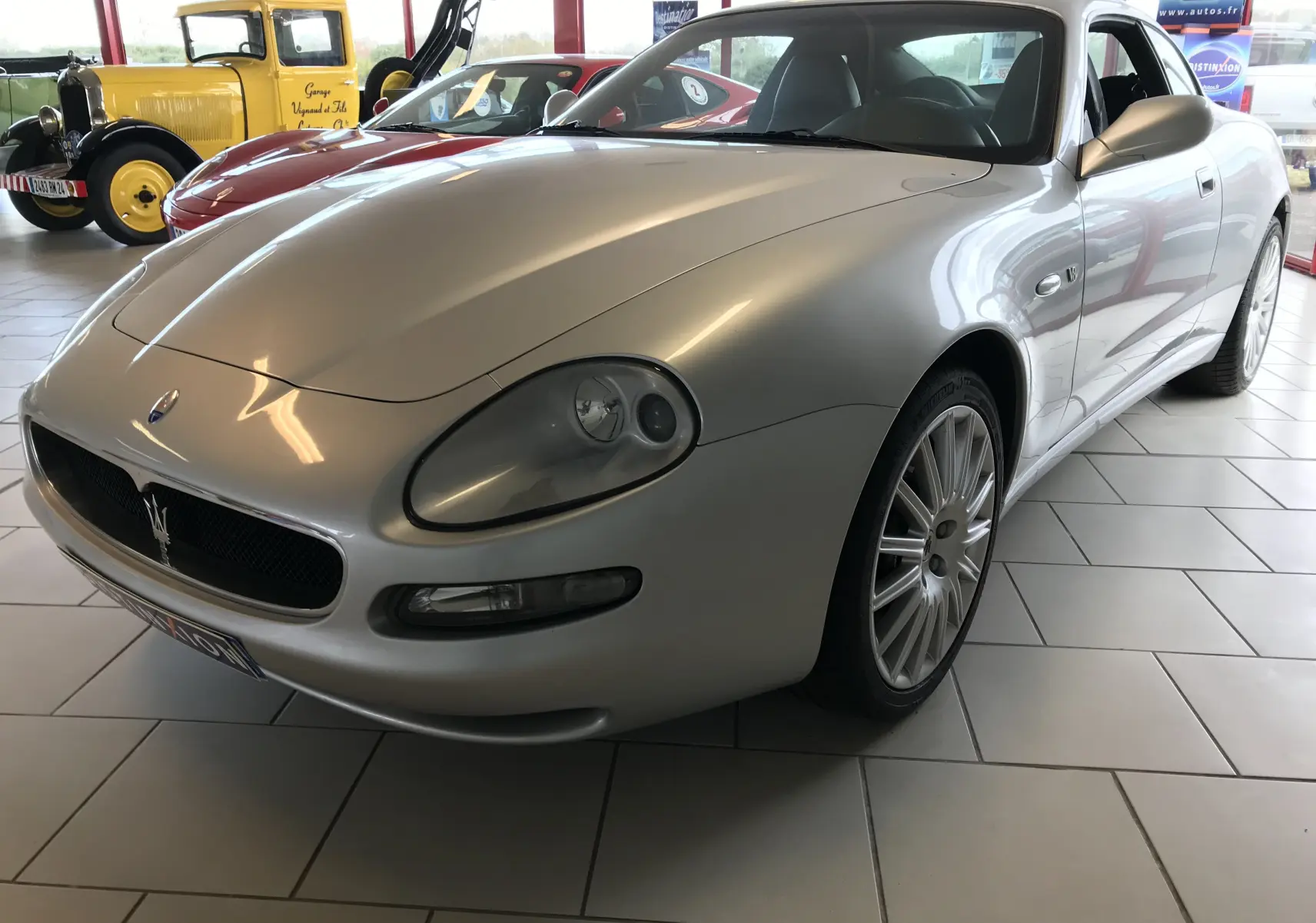 Maserati Coupé gris clair vue 3/4 avant droit, mettant en valeur ses phares ovales et la calandre au trident.
