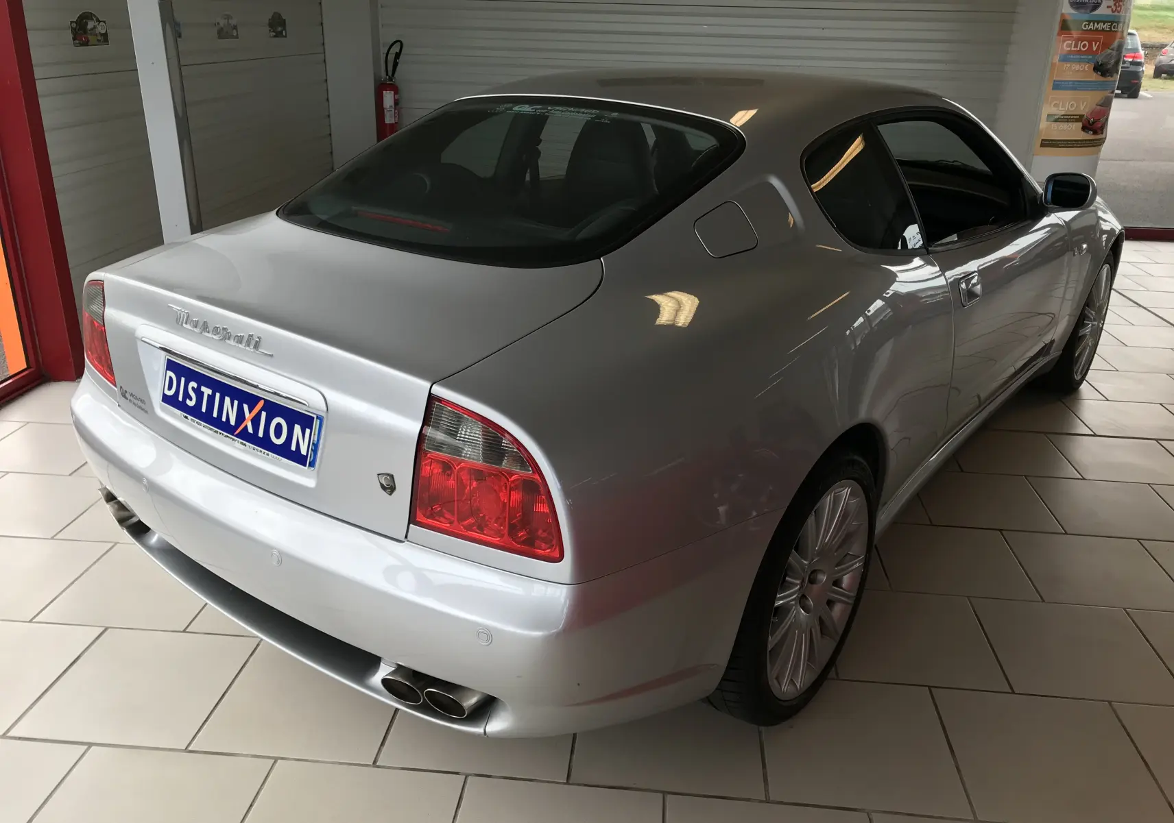 Vue 3/4 arrière droite d'une Maserati Coupé gris clair 2003 avec feux arrière rouges et double sortie d'échappement chromée.