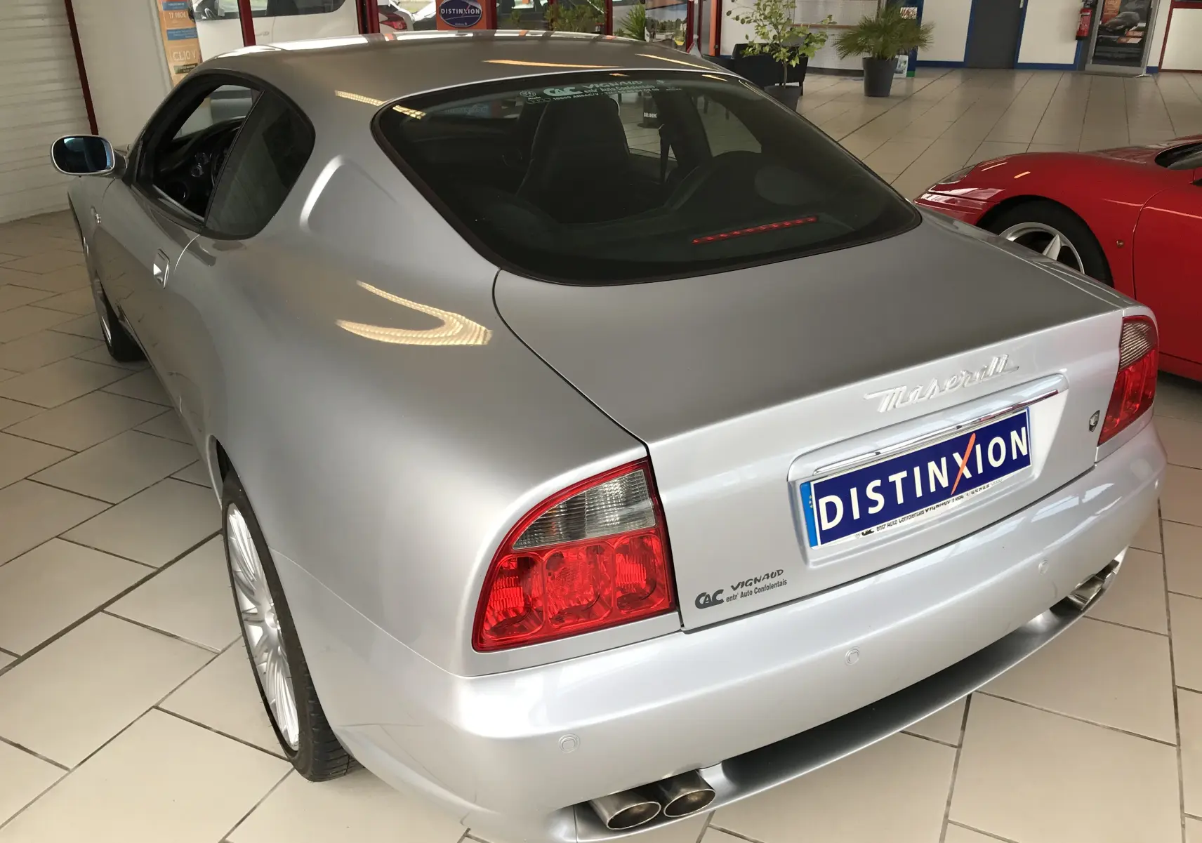Vue 3/4 arrière droite d'une Maserati Coupé gris clair de 2003 avec double sortie d'échappement et feux arrière rouges.