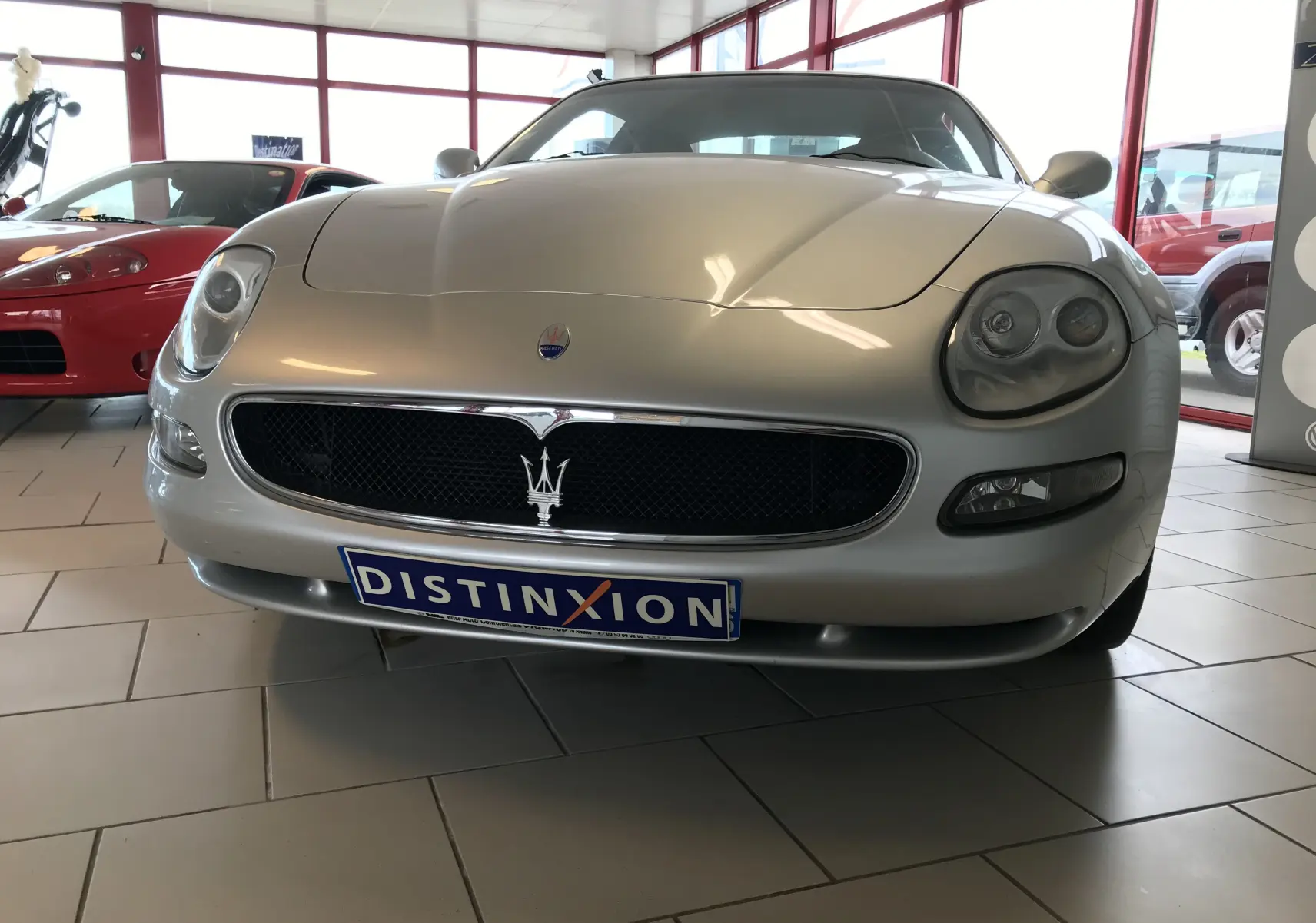 Vue de face d'une Maserati Coupé gris clair de 2003 avec calandre noire et logo trident bien visible.