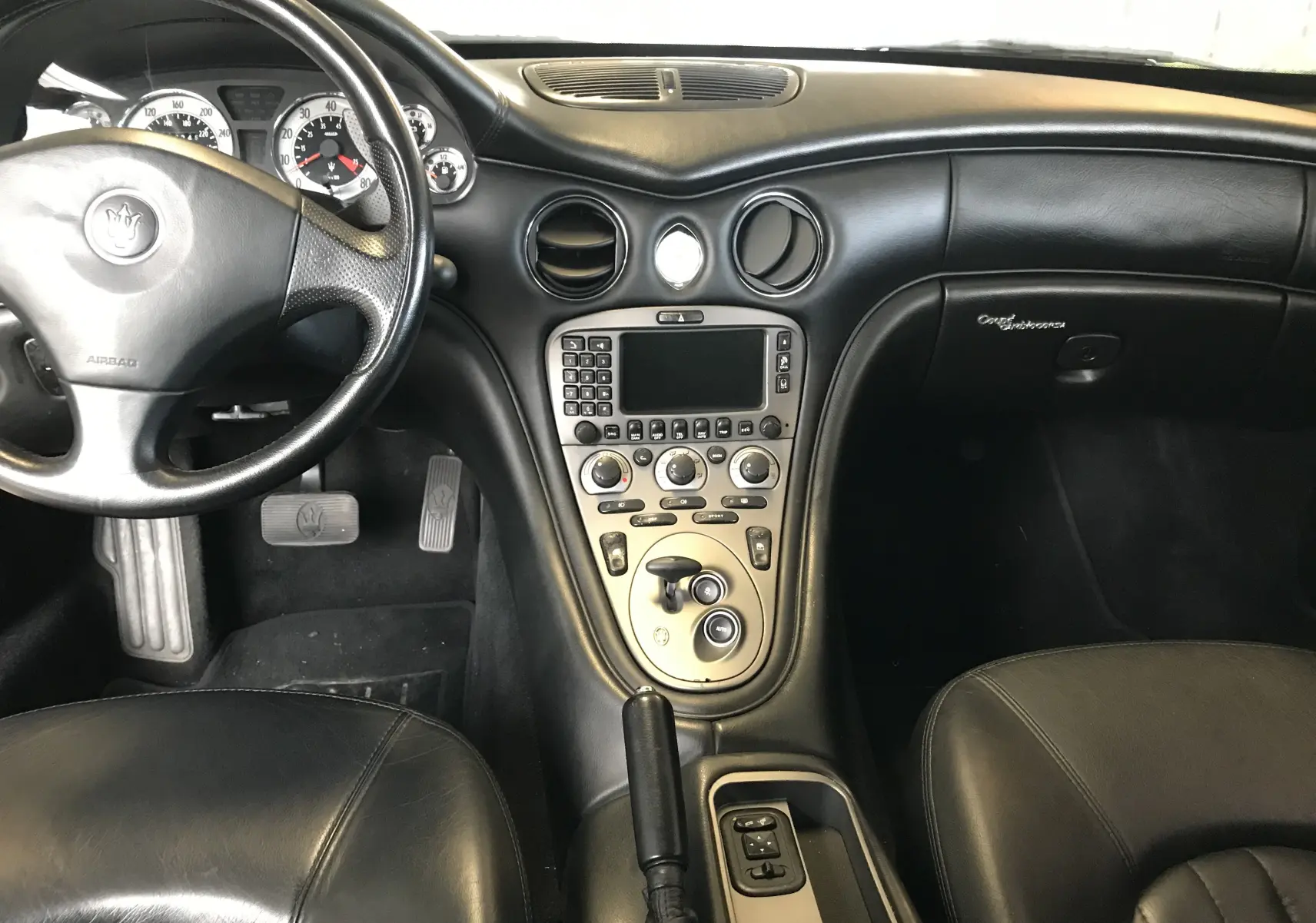 Intérieur noir cuir de la Maserati Coupé 2003, vue centrée sur le tableau de bord et la console centrale.