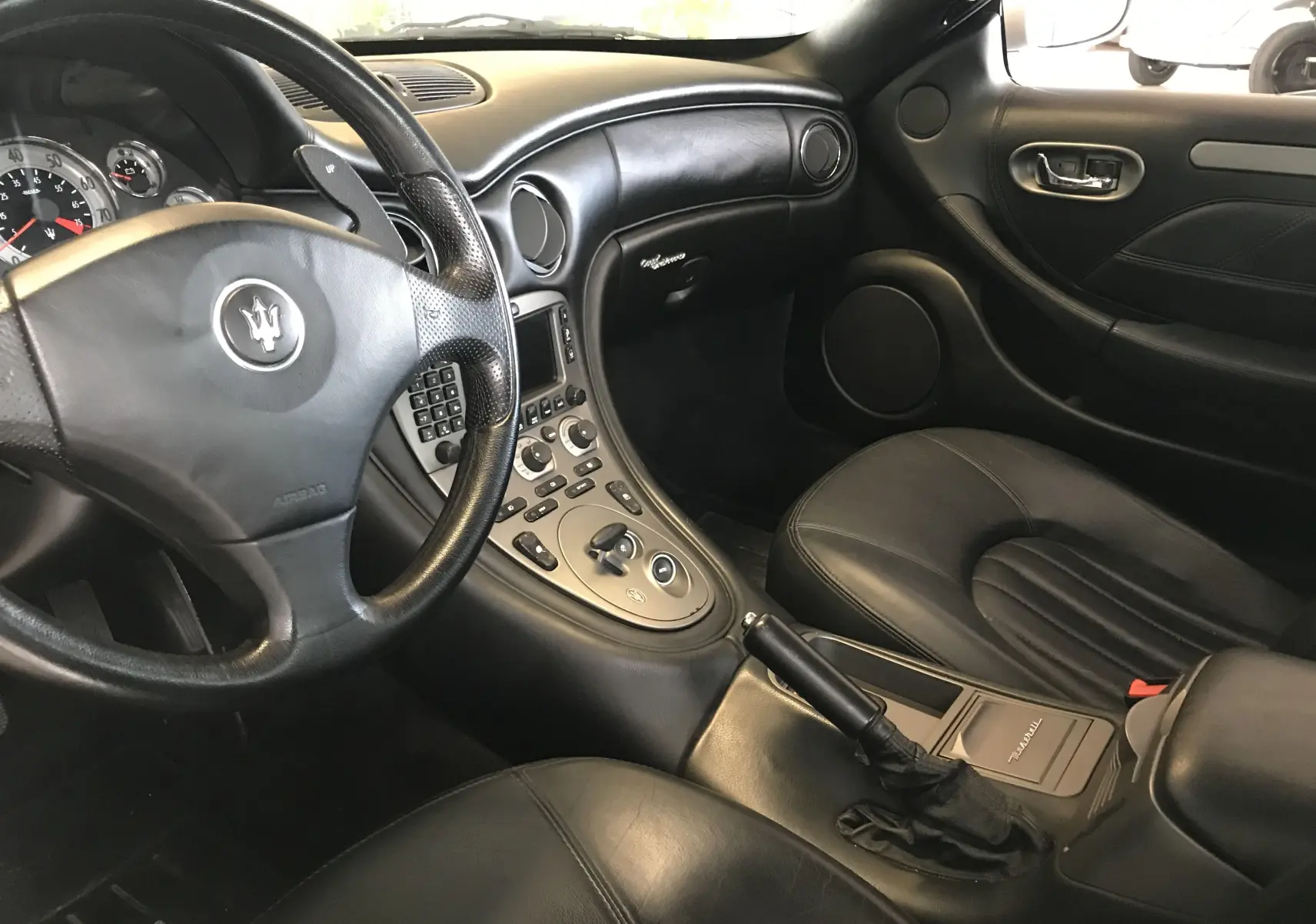 Intérieur noir cuir de la Maserati Coupé 4.2l V8 2003, vue côté conducteur avec tableau de bord et console centrale visibles.