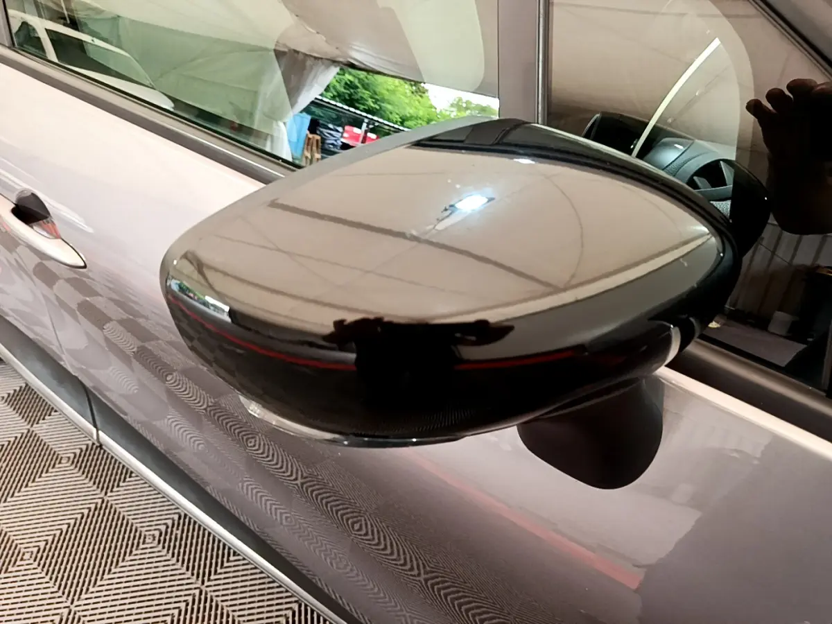 Gros plan sur le rétroviseur côté gauche noir brillant du Renault Captur gris foncé, avec reflet de l'environnement intérieur.