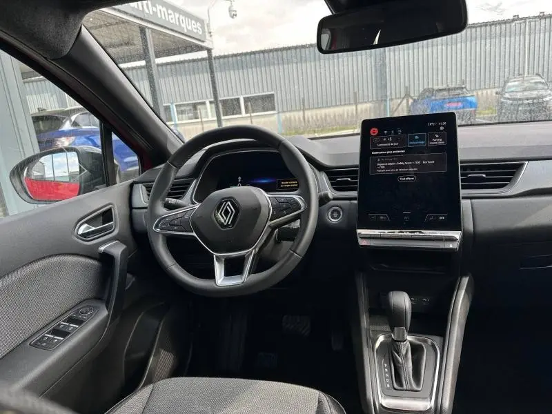 Vue intérieure avant du Renault Captur rouge, montrant le volant multifonction et l'écran tactile central vertical.
