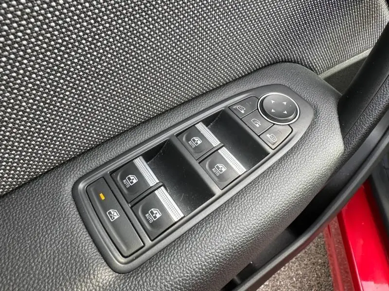 Gros plan sur les commandes des vitres électriques côté conducteur du Renault Captur rouge, avec tissu gris en arrière-plan.