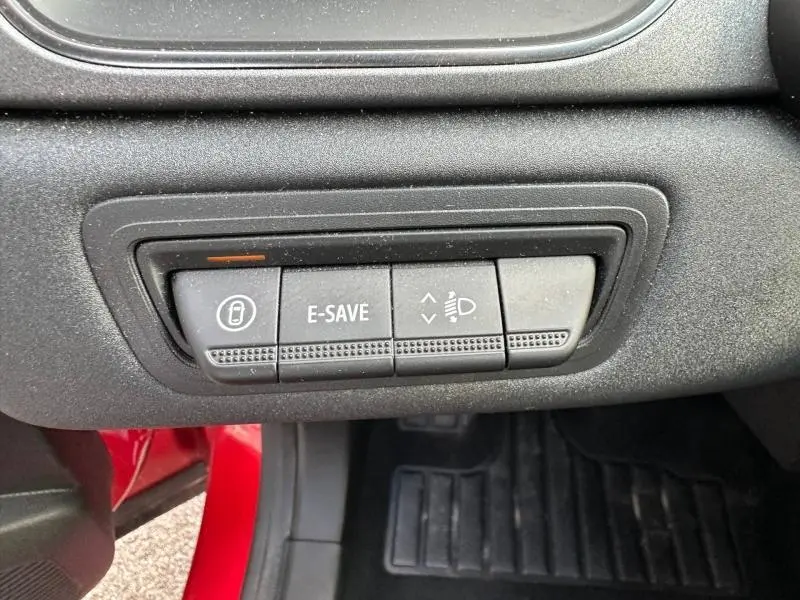 Gros plan sur les commandes situées sous le tableau de bord d’un Renault Captur rouge, avec bouton E-SAVE et réglage des phares.