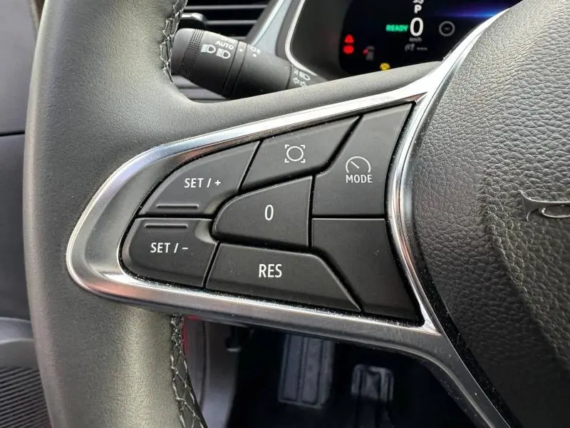 Gros plan sur les commandes multifonctions noires du volant du Renault Captur rouge, avec finition chromée autour.