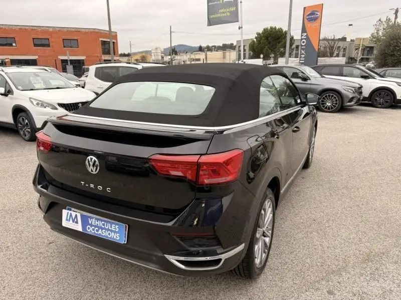 Volkswagen T-Roc Cabriolet noir métal, vue 3/4 arrière droite, capote fermée, détails chromés et feux rouges visibles.
