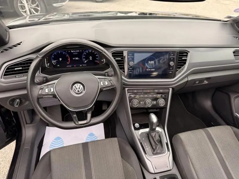 Vue intérieure du tableau de bord et volant du Volkswagen T-Roc Cabriolet noir métal, avec écran tactile et commandes au volant.