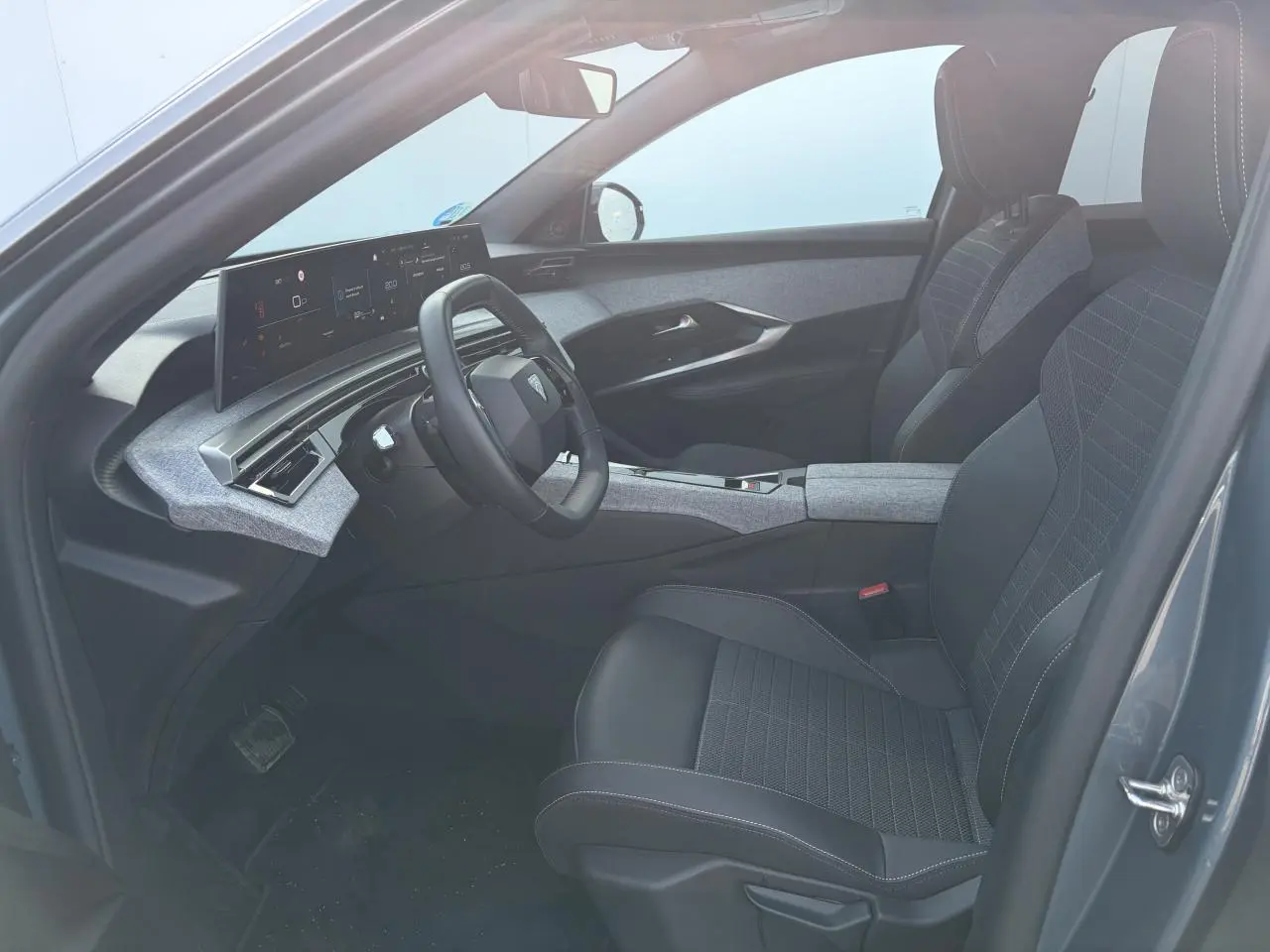 Intérieur avant droit du Peugeot 3008 bleu Ingaro 2024, avec tableau de bord i-Cockpit panoramique et sellerie tissu gris et noir.