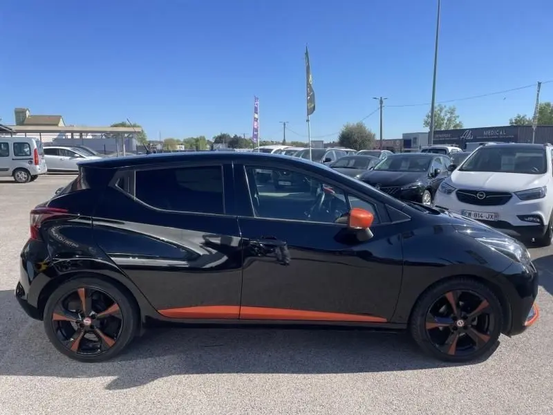 Vue de profil côté gauche d’une Nissan Micra noire avec détails orange sur les jantes et les rétroviseurs.