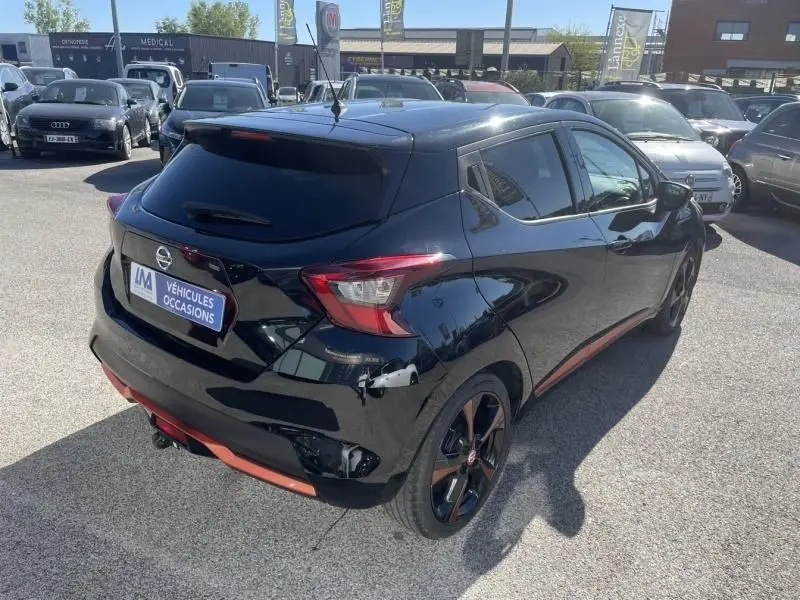 Vue 3/4 arrière droite d'une Nissan Micra noire 2017 N-Connecta avec jantes noires et détails rouges, stationnée en extérieur.
