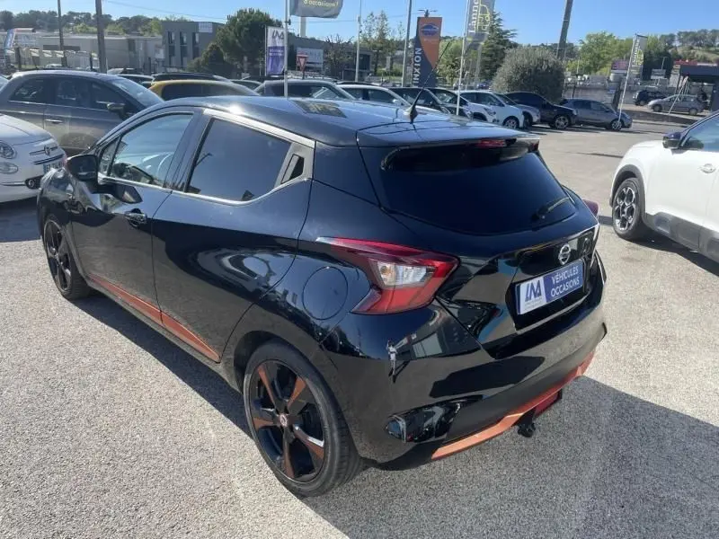 Vue 3/4 arrière droite d'une Nissan Micra noire 2017 avec jantes et détails orange, stationnée en extérieur.