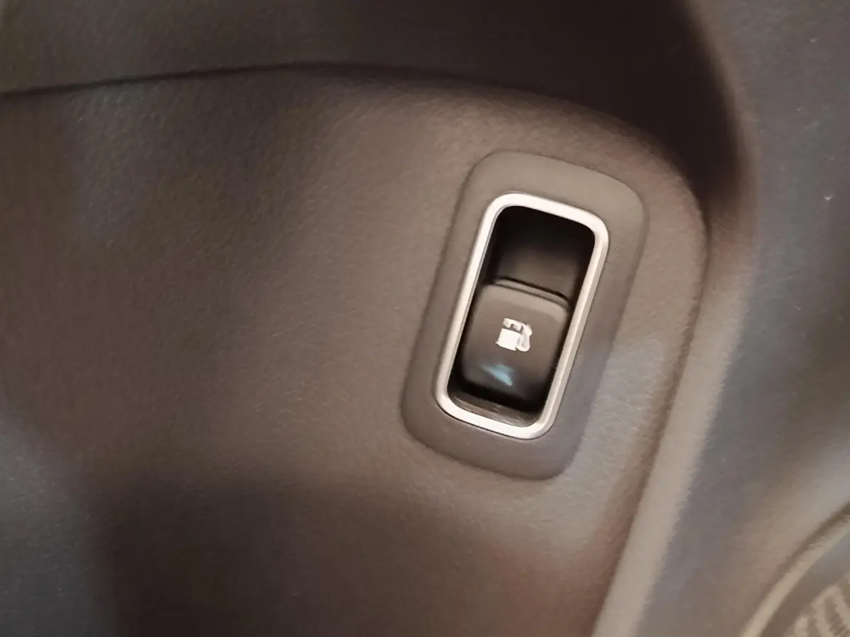 Gros plan sur le bouton d'ouverture de trappe à carburant dans l'habitacle du Mercedes GLA 250 e gris foncé.