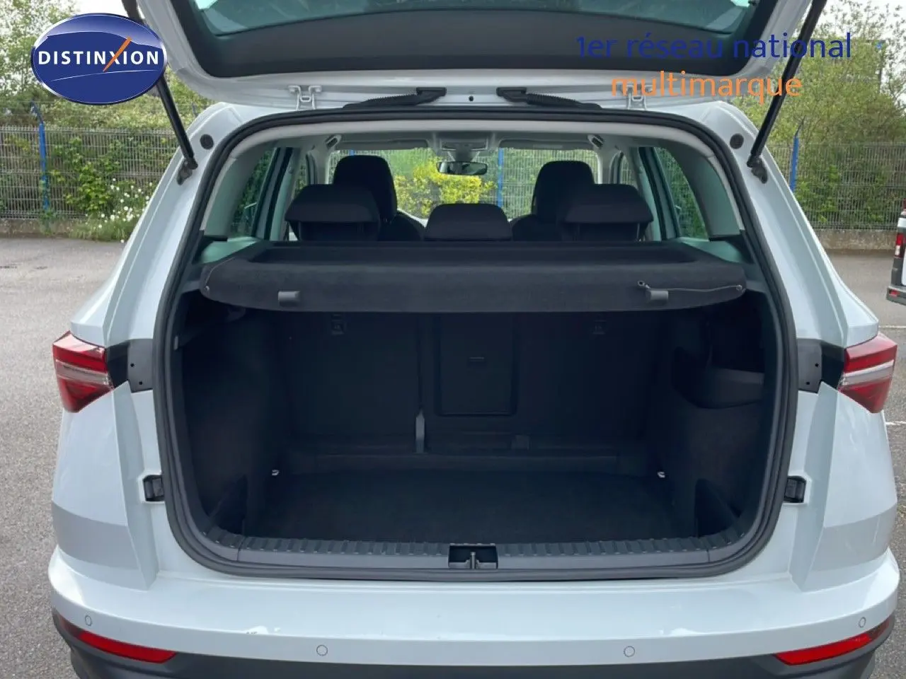 Vue arrière ouverte du coffre d'un Skoda Karoq blanc glacier 2025, montrant l'espace de chargement et la plage arrière noire.