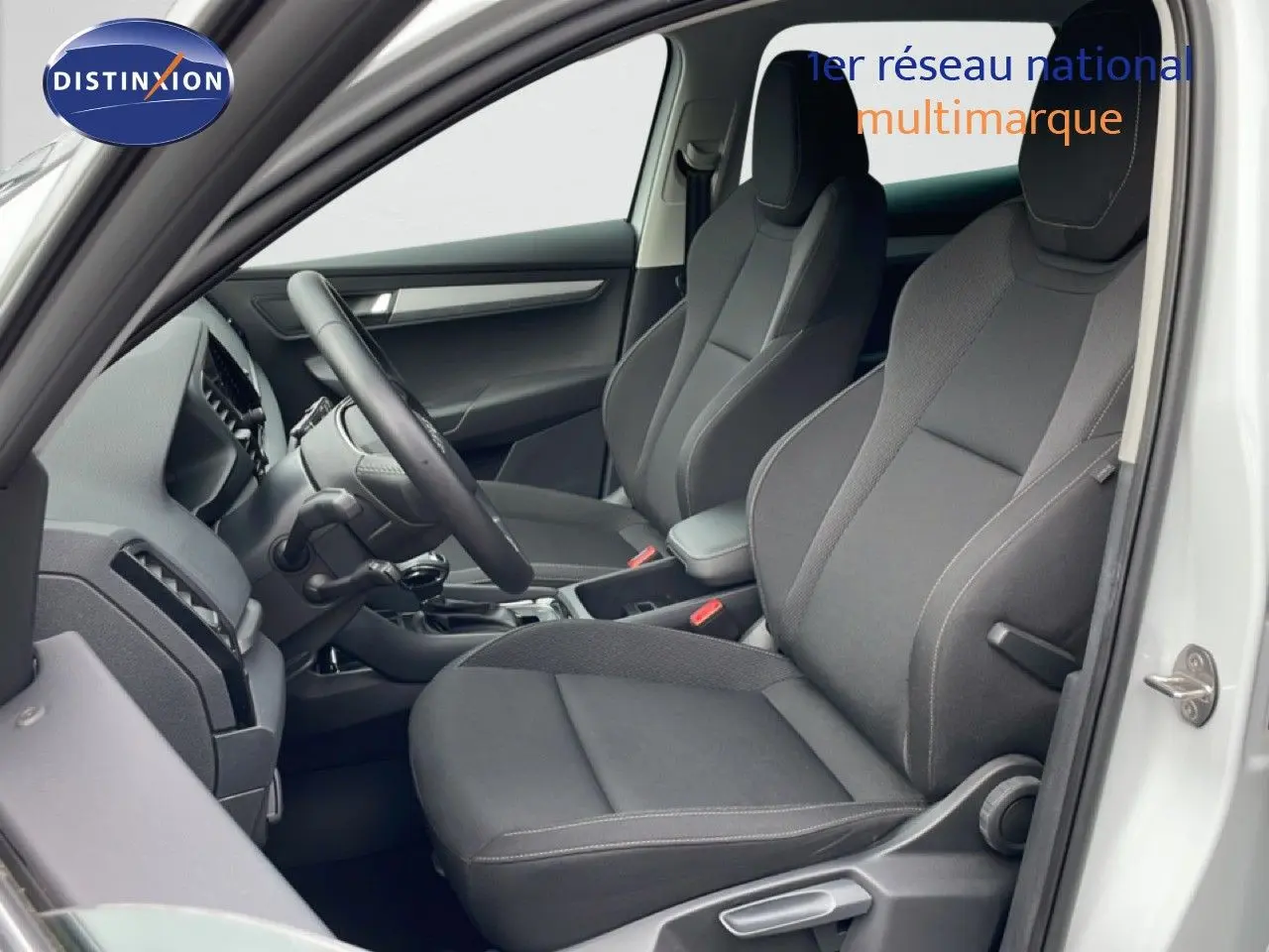 Vue intérieure côté conducteur du Skoda Karoq blanc glacier 2025, sièges tissu gris avec coutures contrastées.
