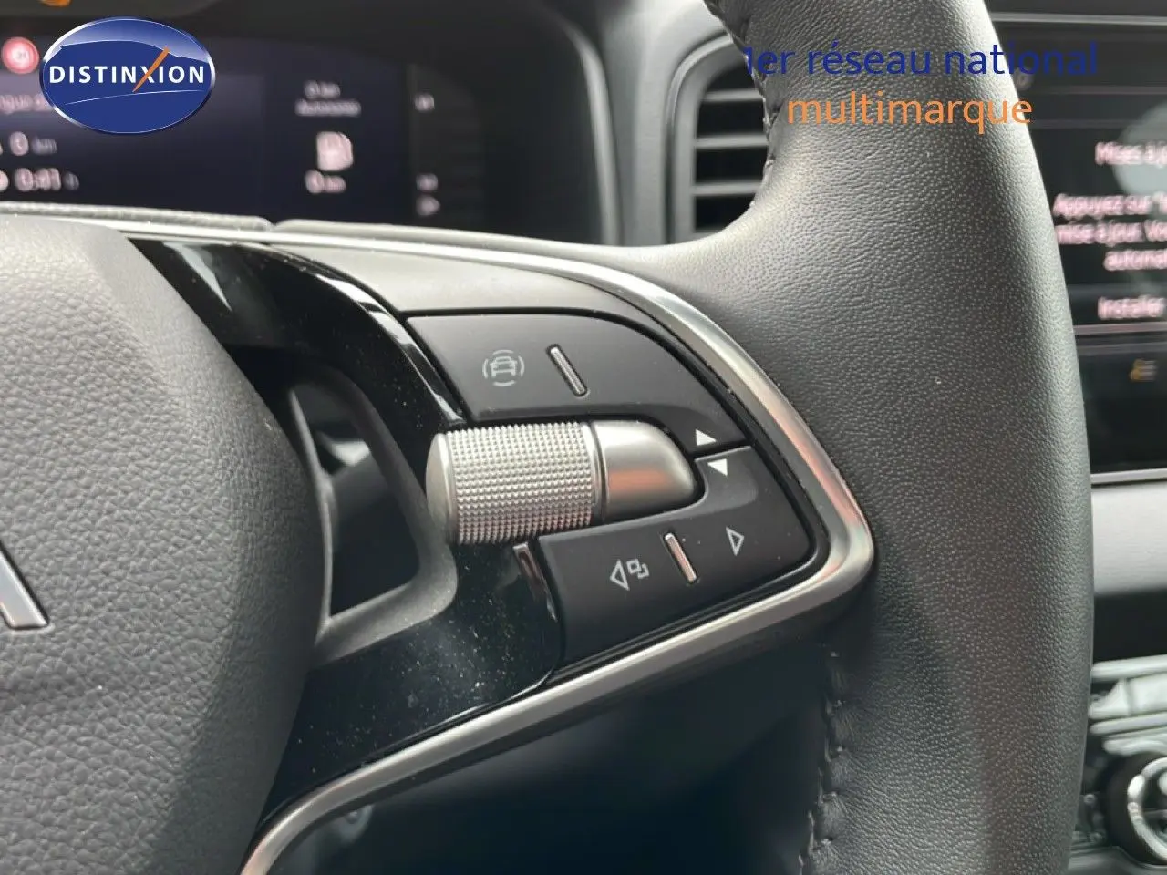 Gros plan sur les commandes au volant en cuir noir du Skoda Karoq blanc glacier, avec tableau de bord numérique en arrière-plan.