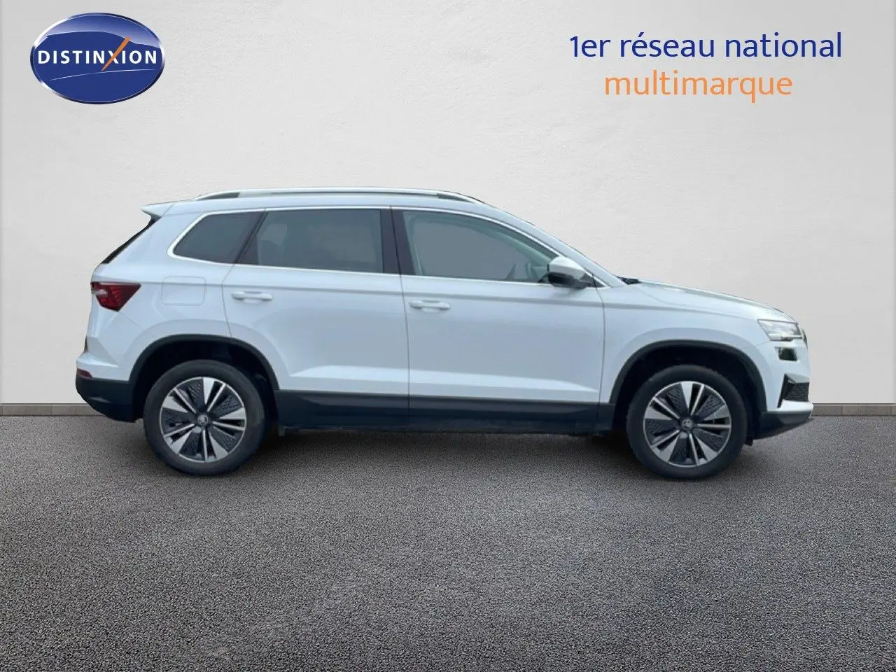 Vue de profil côté gauche d’un Skoda Karoq blanc glacier 2025 avec jantes bi-ton et barres de toit.