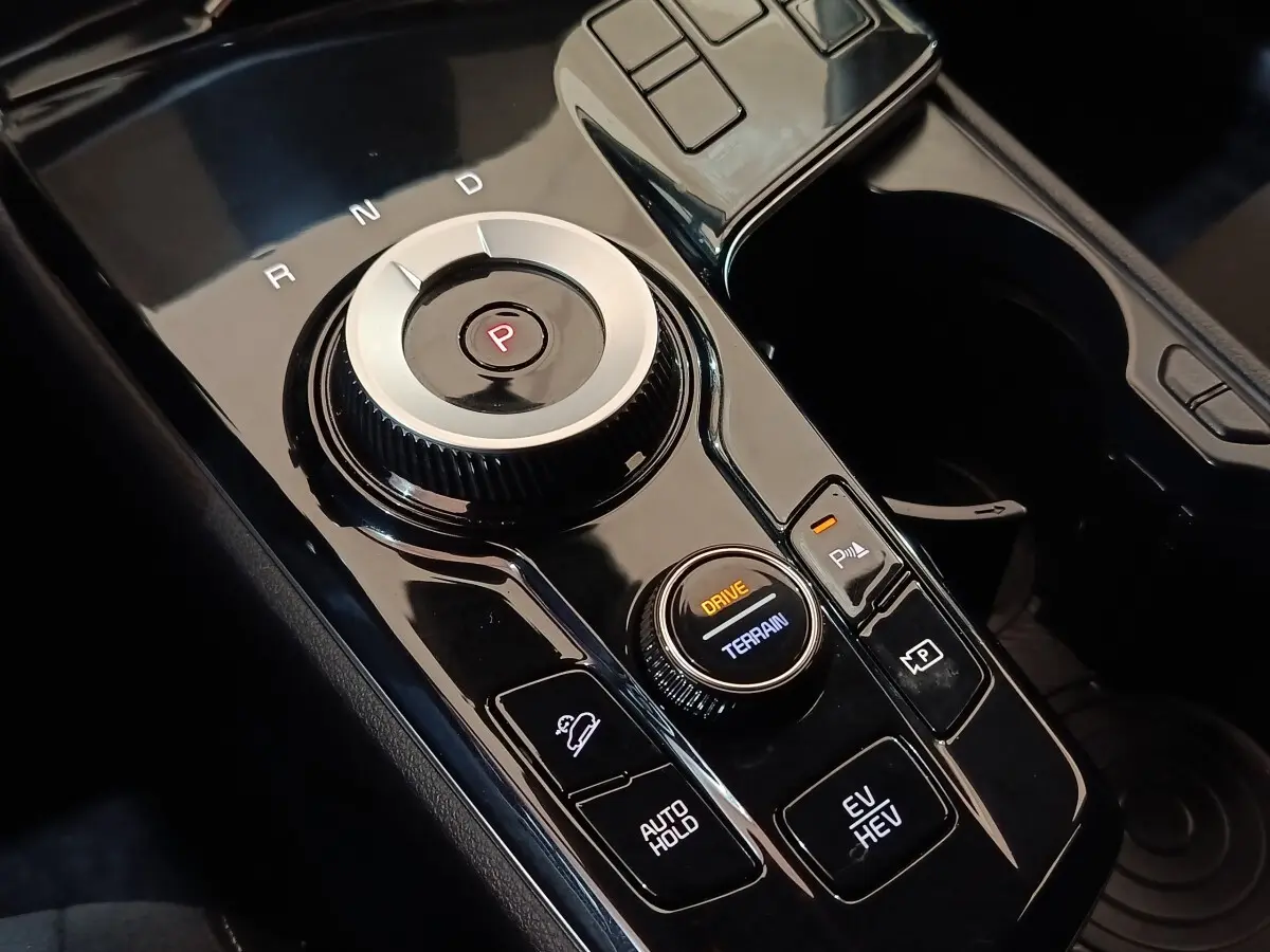 Gros plan sur la console centrale noire du KIA SPORTAGE hybride rechargeable avec sélecteur de mode de conduite et bouton de frein à main.